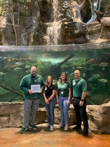 two men and two women post in front of a large fish tank with a waterfall inside of Bass Pro Shops in Portage, Indiana.